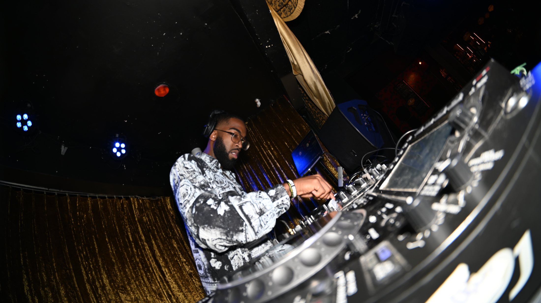 THA PRFSSR at the decks under club lights, a gold curtain behind